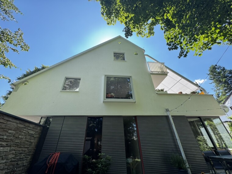Ansicht der hellen Giebelfassade mit Fenstern, Balkon und dunkler Verkleidung im Erdgeschoss.