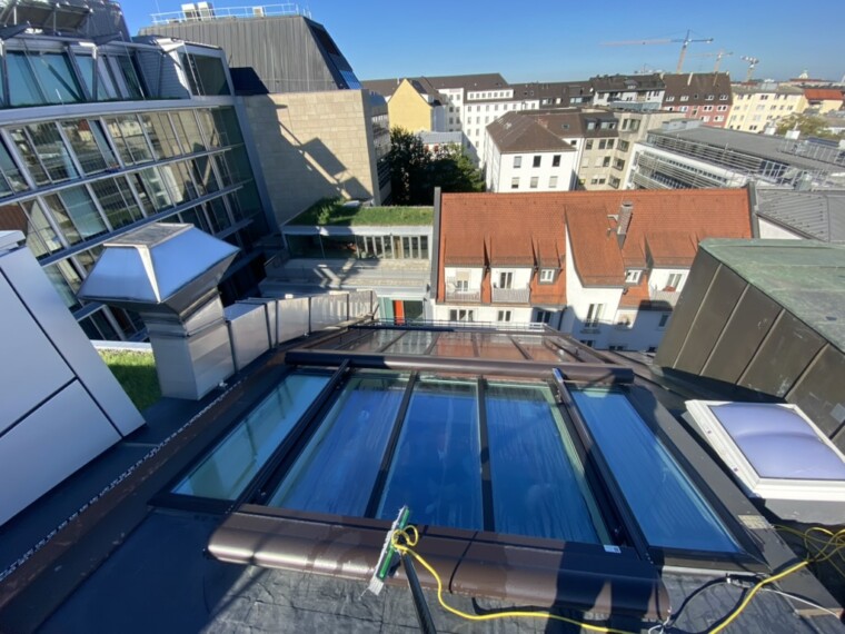 Blick von oben auf eine Dachverglasung mit braunen Profilen; am unteren Rand liegen eine Reinigungsbürste und ein gelber Schlauch.