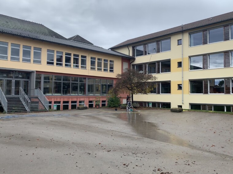 Fensterreinigung mit einer Teleskopstange an einem mehrgeschossigen Gebäude, aufgenommen vom Innenhof