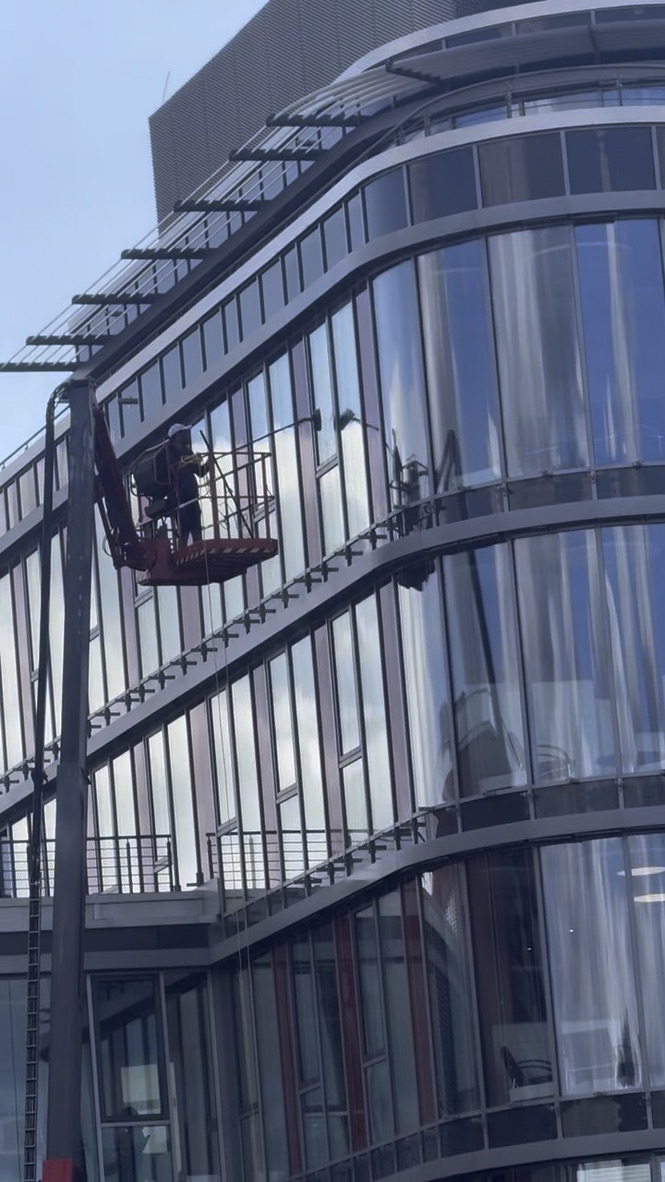Mitarbeiter in einer roten Arbeitsbühne bei der Reinigung einer gebogenen Glasfassade.