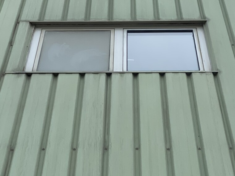 Industriefenster in einer grünen Profilfassade mit einer trüben linken und einer klareren, spiegelnden rechten Scheibe
