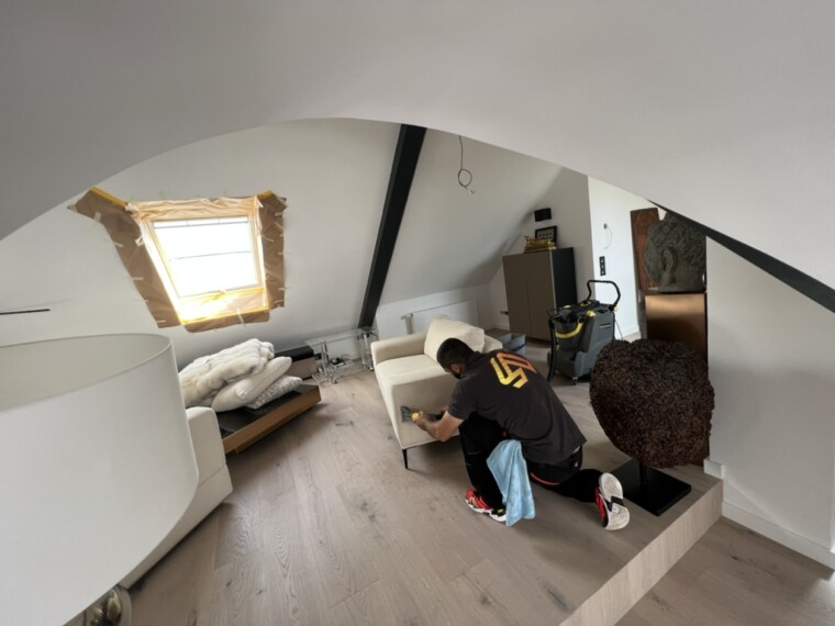 Alpin-Mitarbeiter bei der Reinigung eines hellen Polstersessels in einem Dachgeschossraum