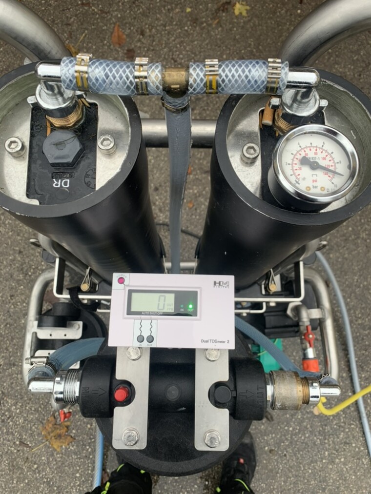 Wasseraufbereitungssystem mit Filtergehäusen, Schläuchen, Manometer und digitalem TDS-Messgerät; das Display zeigt 0