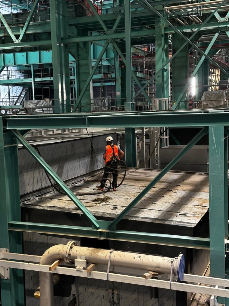 Reinigungsarbeit zwischen grünen Stahlträgern in einem Industriebereich.